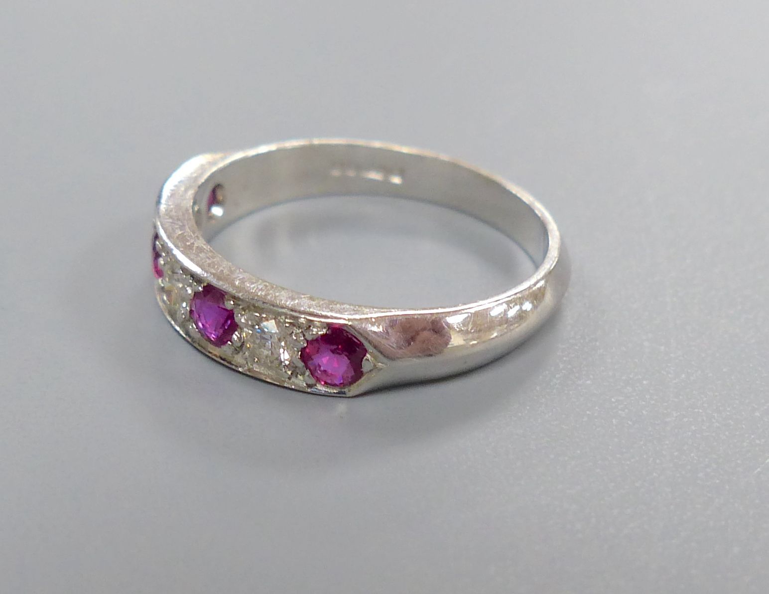 A modern 18ct white gold, four stone ruby and three stone diamond set half hoop ring, size M, gross 3.7 grams.